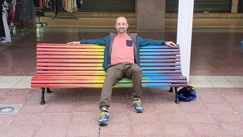 Miguel sentado en un banco con la bandera gay en 2022
